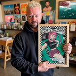 Load image into Gallery viewer, A man holding a framed comic book titled "BOMBSHELL" in a room filled with various artworks and memorabilia.
