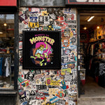 Load image into Gallery viewer, a wall covered in a collage of various stickers, posters, and graffiti, creating a visually busy and chaotic appearance.
