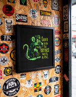 Load image into Gallery viewer, a wall covered in various stickers, patches, and graffiti, including a framed image of a rat with a humorous caption.
