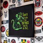 Load image into Gallery viewer, a wall adorned with a variety of stickers, patches, and graffiti, including a framed image of a cartoon rat with a humorous caption.
