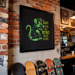 Load image into Gallery viewer, a framed poster of a rat with a humorous caption, hanging on a brick wall. Below the poster, there are several skateboards lined up, suggesting a skateboard shop or a skate park.
