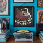 Load image into Gallery viewer, a wall with a framed poster of a red boot, surrounded by various CDs and records on a shelf.
