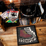 Load image into Gallery viewer, A collection of vinyl records and a turntable on a wooden floor, with a framed poster featuring a shoe and the text "These boots were made for stompin'".
