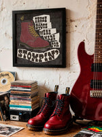 Load image into Gallery viewer, a wall with a framed poster, a stack of CDs, a pair of red boots, and a red electric guitar.
